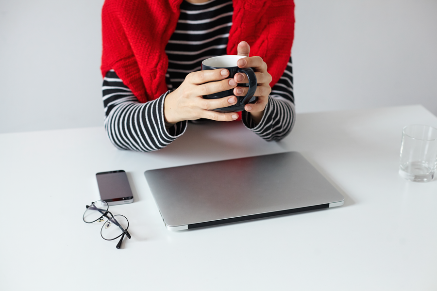 900cropped-photo-of-young-stylish-woman-freelancer-keeping-cup-of-tea-in-her-hands-while-preparing-for-business-meeting-sitting-at-table-with-modern-laptop-and-smartphone